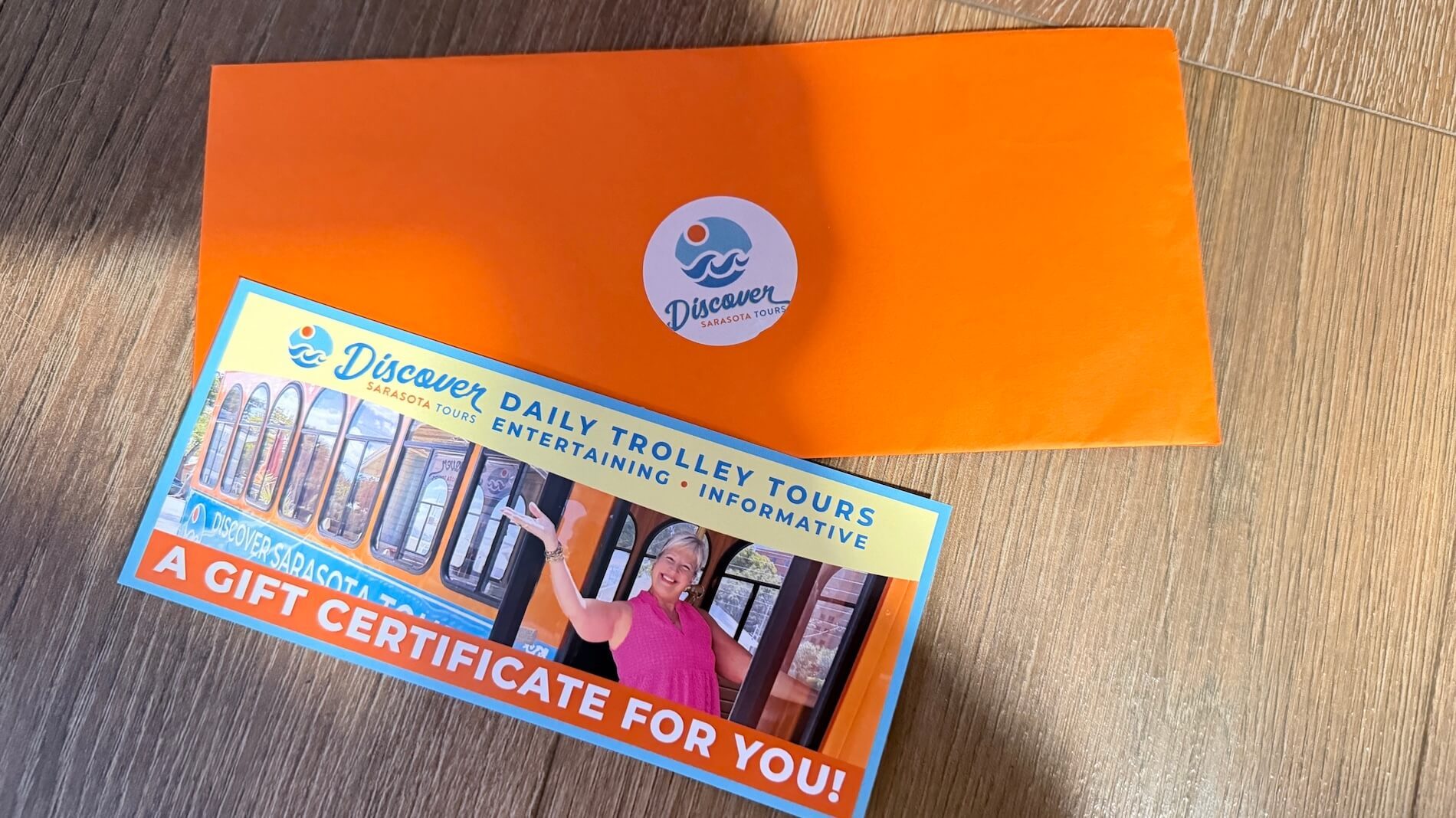 Orange envelope and gift certificate for Discover Trolley Tours on a wooden surface.