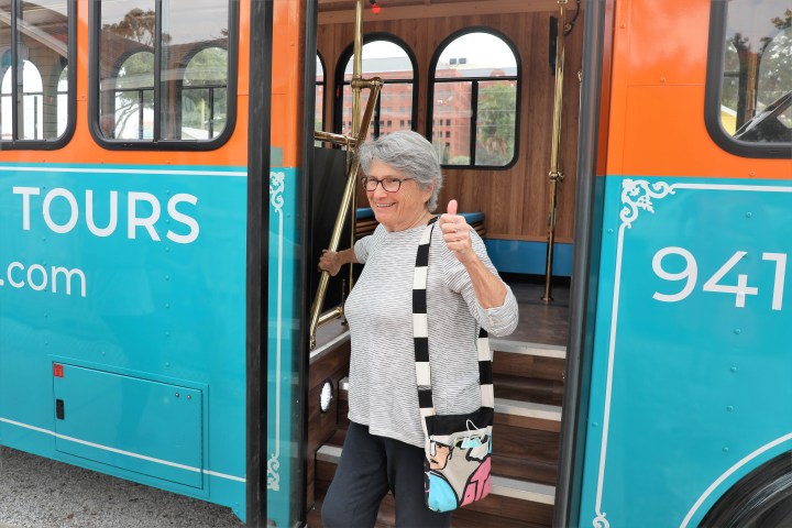 Smiling woman exiting a colorful tour bus with a thumbs-up gesture.