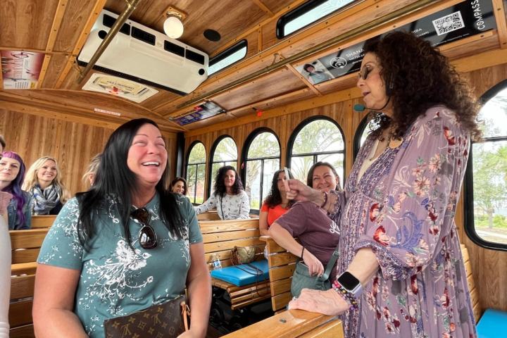A group of women smiling and laughing inside a wooden trolley bus.