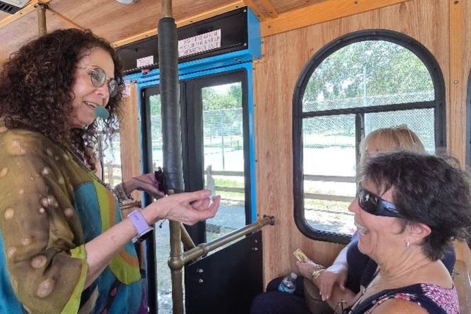 Two women interacting and smiling inside a wooden interior bus with round windows.