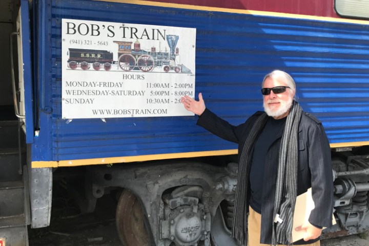 Man with sunglasses standing next to sign on train car.