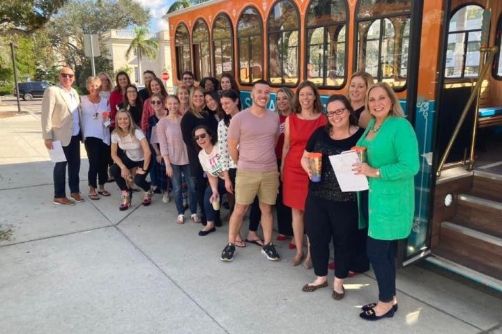 Group of people smiling near a parked orange trolley on a sunny day.