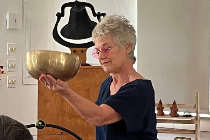 Woman with short gray hair holding a brass bowl indoors.