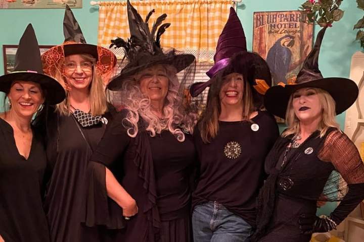 Five people in witch costumes and hats smiling indoors.