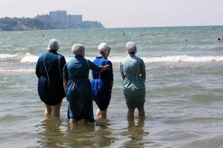 Four people in traditional dresses and bonnets standing in the sea.