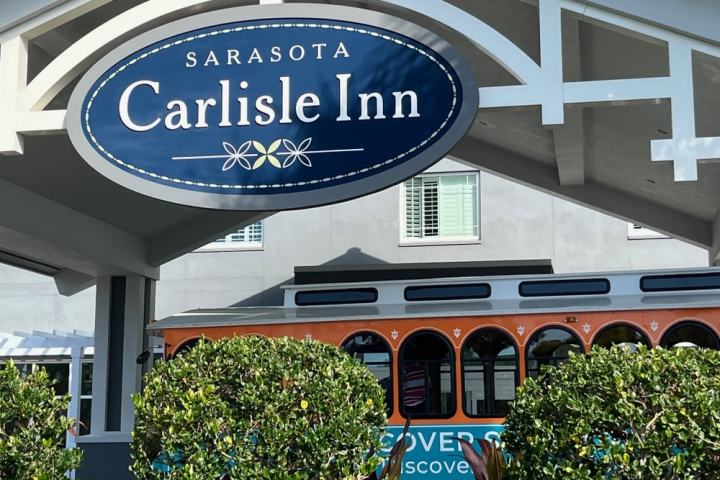 Sign reading 'Sarasota Carlisle Inn' with trolley and greenery in background.