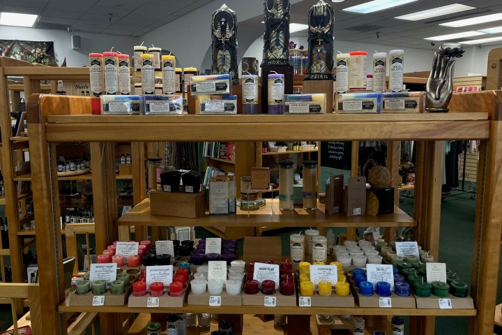 Wooden shelves display colorful candles, sculptures, and glass jars in a store setting.