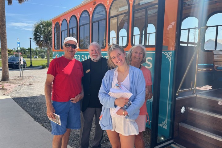 Four people smiling next to a colorful trolley on a sunny day.