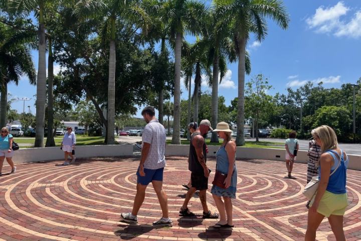 People walking on a brick spiral path under palm trees on a sunny day.