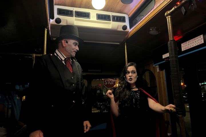 Two people in costumes with face paint stand inside a dimly lit trolley car.