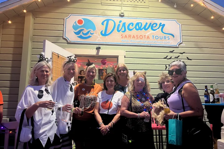 Group of costumed women posing outside a tour building with a 'Discover Sarasota Tours' sign.