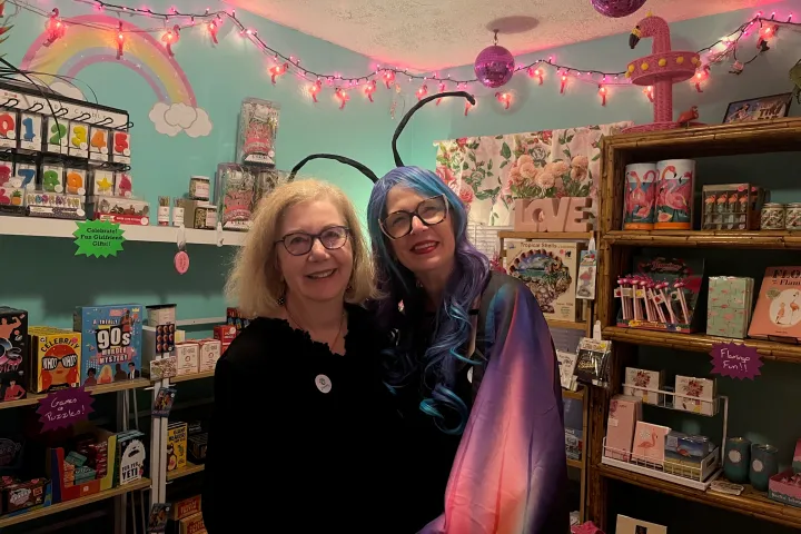 Two women smiling in a colorful store with toys and pink lights.
