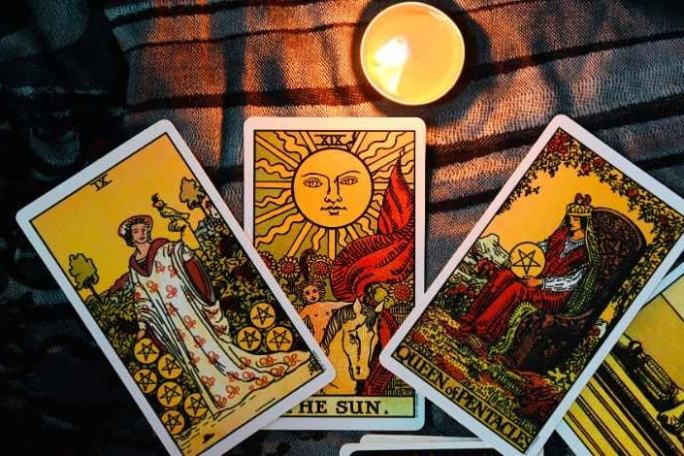 Tarot cards with candle: The Sun, Queen of Pentacles, and a third card, on a patterned cloth.