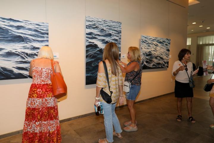 People viewing ocean-themed paintings in an art gallery.