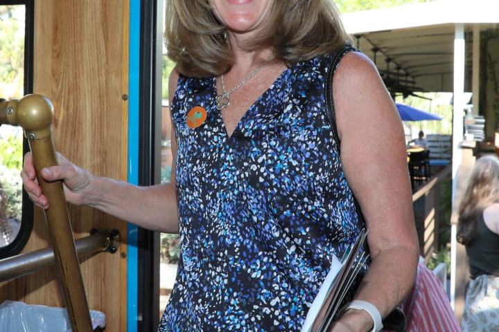 Smiling woman in sunglasses holding papers, entering a trolley bus.