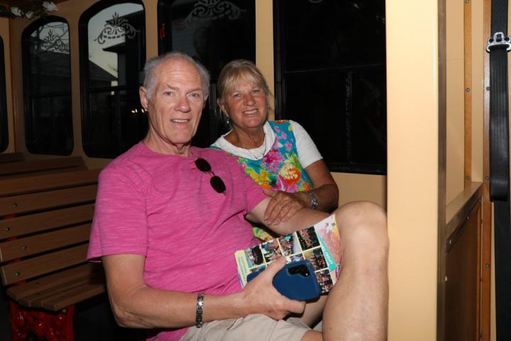 Two people sitting inside a trolley holding a brochure and smartphone, with wooden benches and windows visible.