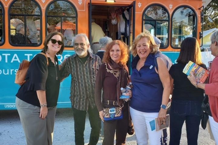 Group of people smiling in front of a tourist trolley on a sunny day.