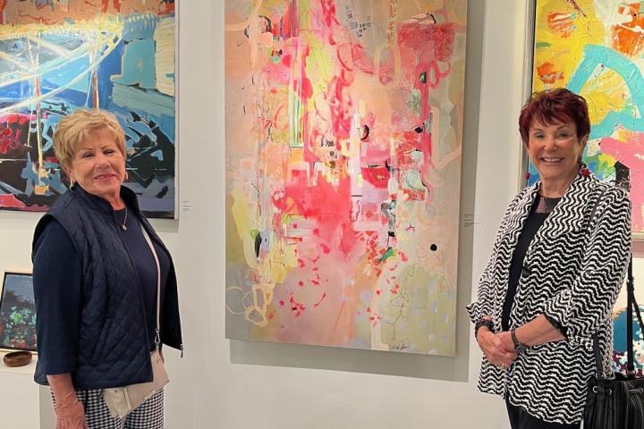 Two women standing in an art gallery beside colorful abstract paintings.