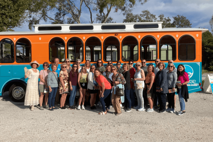 Group of people posing in front of a colorful trolley bus in a park.