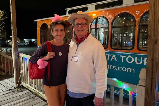 Two people in costumes stand in front of an orange tour bus at night.