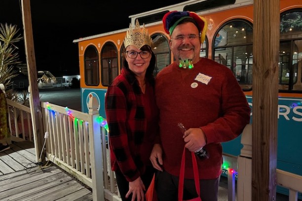 Two people wearing festive hats stand in front of an orange trolley at night.