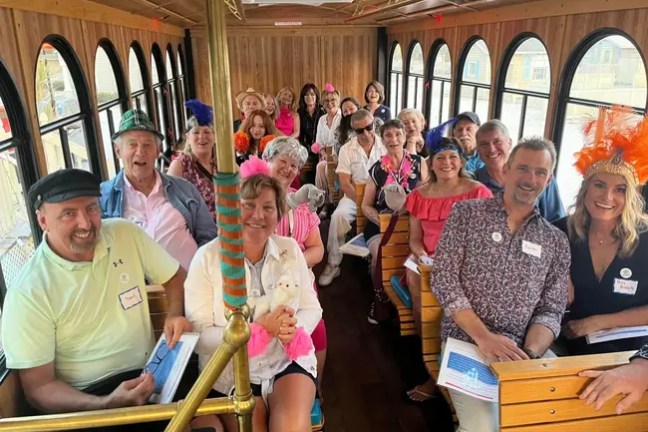 A group of people wearing festive hats sit inside a wooden trolley.