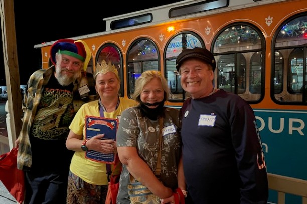 Four people smiling in front of an orange trolley at night.