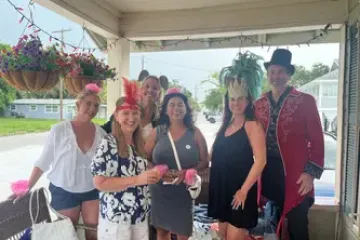 Group of people in costumes smiling on a porch with potted plants and summer attire.