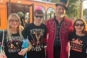 Four people smiling outdoors, wearing circus-themed attire near an orange streetcar.