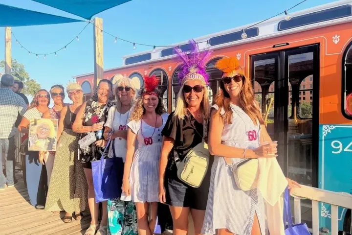 Group of people in festive attire posing in front of an orange tram on a sunny day.