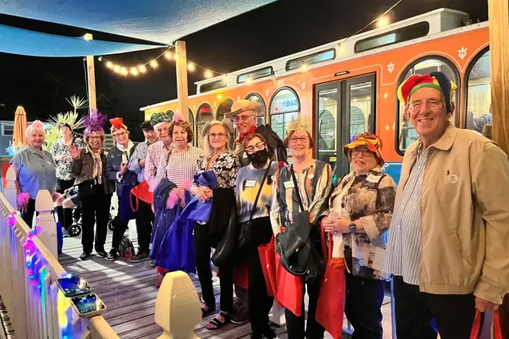 Group of people in festive attire posing in front of a trolley at night.