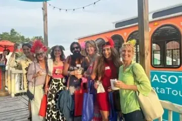 Group of people in colorful outfits posing with drinks near an orange bus.