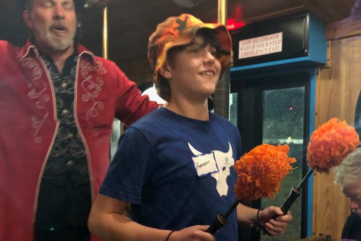 Two people on a bus, one with pom-poms and a bucket hat.