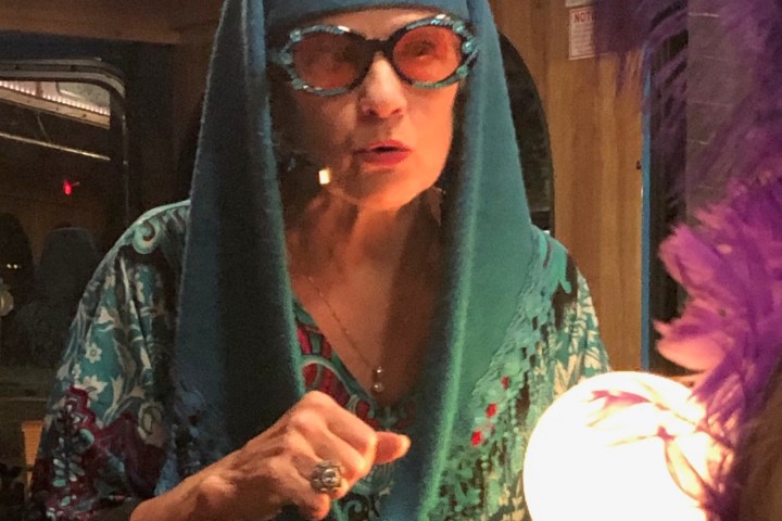 Woman in blue attire holding a glowing orb, wearing ornate glasses and headpiece indoors.