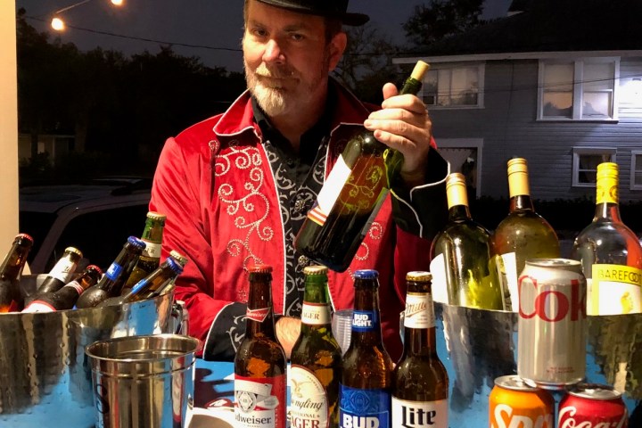 Man in top hat behind a bar with various beer and soda bottles at night.