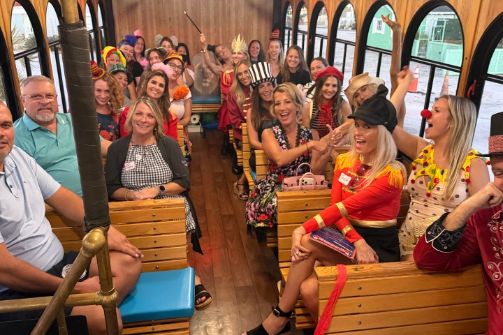 People in costumes sitting inside a wooden trolley, smiling and posing for a photo.