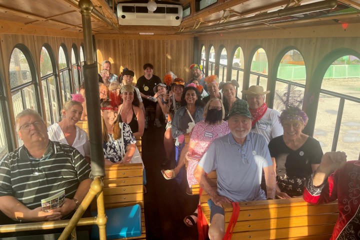 group of MURDER trolley guests posing for the camera in costume while sitting on the trolley