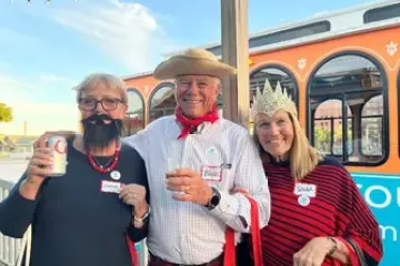 Three people in costumes smiling, one with a fake beard, near a trolley.