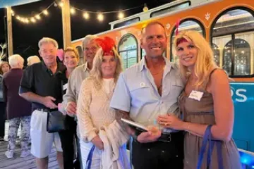 Group of people smiling outside a trolley at night, some wearing feather headbands.