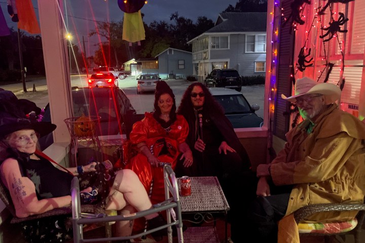 Four people in Halloween costumes sitting on a porch with lights and decorations.