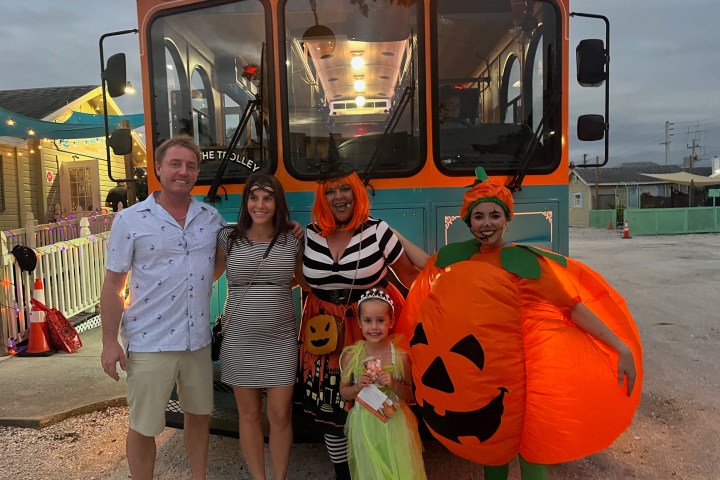Group in costumes standing in front of an orange trolley at dusk.