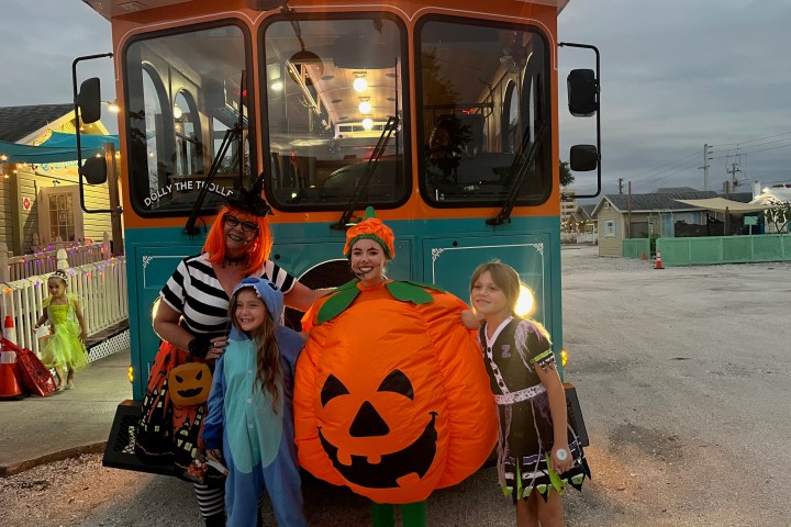 People in Halloween costumes pose in front of a trolley decorated with lights.
