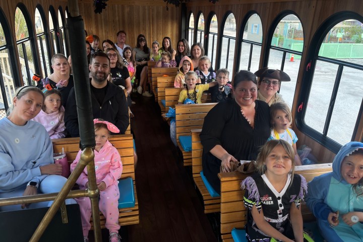 A group of adults and children in costumes seated inside a trolley.