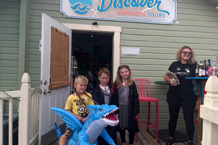 Three kids in costumes pose with a woman outside Discover Sarasota Tours entrance.