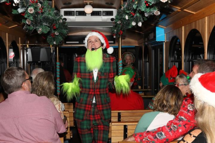 Man in green beard and Santa hat performs on a decorated Christmas bus.
