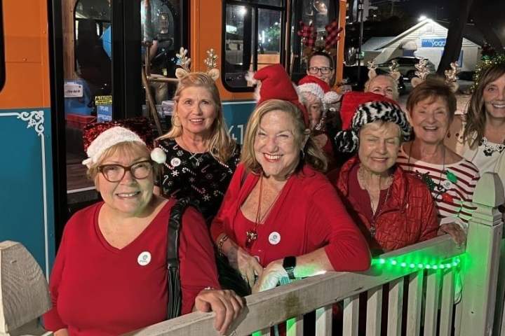 Group of women in festive attire smiling outside a decorated bus at night.
