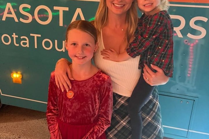 Three people posing in front of a tour bus at night, with holiday lights reflecting on the windows.