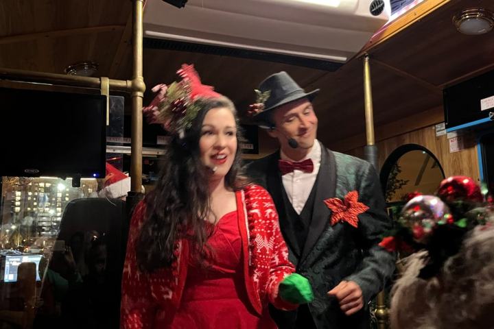 Two people in festive attire on a bus, wearing microphones and holiday decorations.