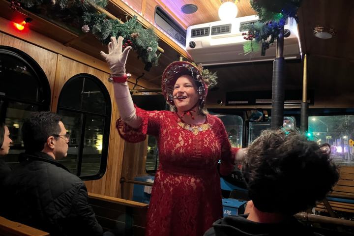 Woman in festive attire speaking to passengers on a decorated bus.