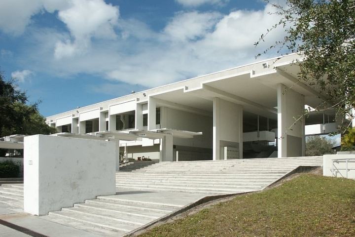 Modern white building with large overhangs and wide steps, under a partly cloudy sky.